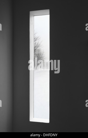 Mit Blick auf verschneite Winterlandschaft draußen vor dem Fenster eines dunklen Raumes. Stockfoto