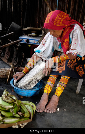 Eine indigene Guna-Frau in traditioneller Kleidung, die in ihrer Küche auf der Insel Carti Sugtupu in der Comarca (Region) der Guna Yala-Ureinwohner, bekannt als Kuna, frische Kokosnuss zerkleinert, die sich im Archipel der San Blas Blas-Inseln im Nordosten Panamas mit Blick auf das Karibische Meer befindet. Stockfoto