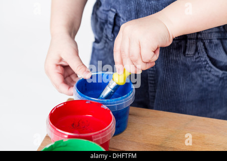 Kind hält Pinsel in blauer Farbe Wanne Stockfoto