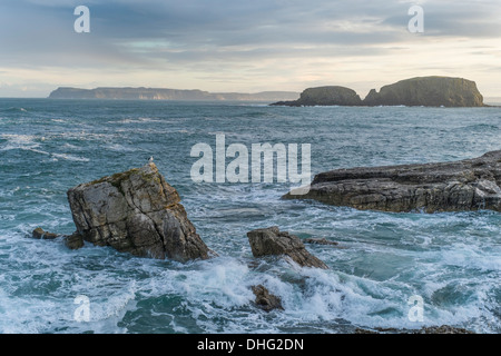 Rathlin Island in der Ferne wie aus Ballintoy mit abgehackt Meere und Felsen im Vordergrund zu sehen. Stockfoto