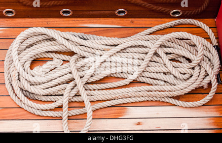 Marine Seil aufgewickelt auf einem hölzernen Dock und gebunden an ein Metall dock Klampe Stockfoto