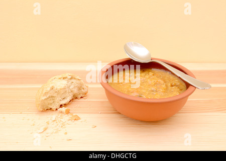 Löffel ruht auf einen Teller Suppe, Rollen mit Hälfte ein knuspriges Brot und Krümel auf dem Tisch Stockfoto