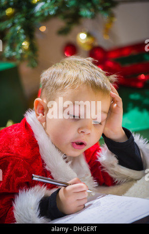 Entzückende 5 jährigen Jungen schreibt an den Weihnachtsmann, Weihnachtsbaum im Hintergrund Stockfoto