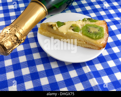 Kiwi lecker Kuchen hautnah am Teller und Champagner Flasche Stockfoto