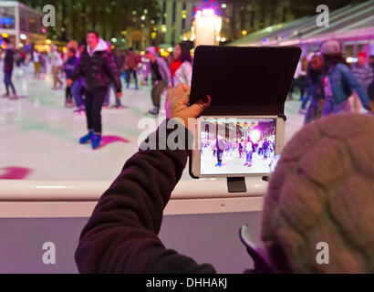 Manhattan, New York, USA 9. November 2013. Besucher Mini Tablet iPad nutzt, um Foto von Eisläufern, an Winterdorf Eisbahn im Bryant Park in der Nacht, © Ann E Parry/Alamy, Live-Nachrichten Stockfoto