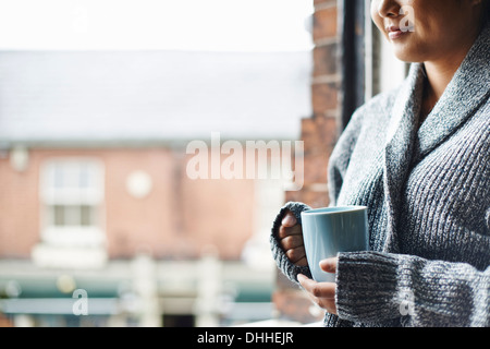 Junge Frau in der Küche hält Becher Kaffee Stockfoto