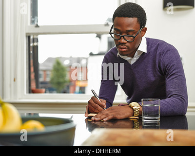 Junger Mann Notizen am Küchentisch Stockfoto