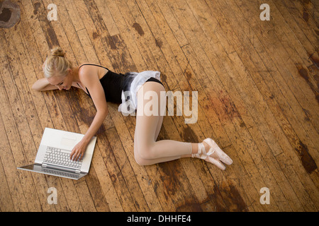 Ballett-Tänzerin liegend auf Holzboden mit laptop Stockfoto