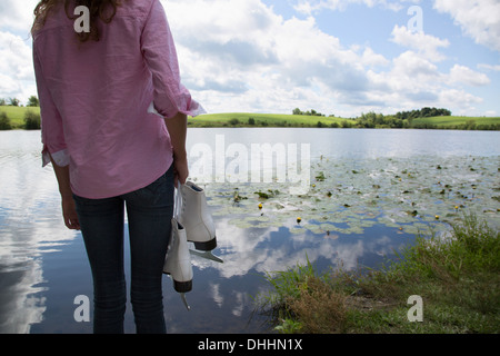 Teenager-Mädchen neben See hält Schlittschuhe Stockfoto