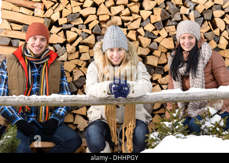 Junge Leute sitzen außen Winter Kleidung Holzscheite im Hintergrund Stockfoto