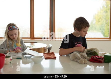 Jungen und Mädchen sitzen am Tisch lesen Stockfoto