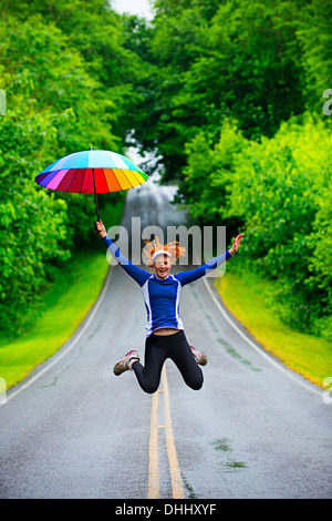 Teenager-Mädchen springen mit Regenschirm auf Straße, Bainbridge Island, Washington, USA Stockfoto