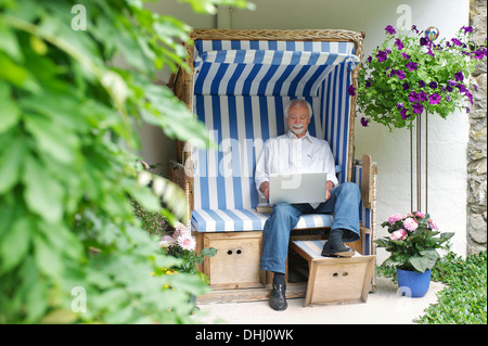 Ältere Mann mit Laptop auf Gartenbank Stockfoto