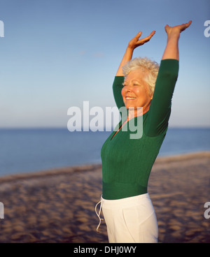 Porträt von schöne Reife Frau praktizieren Yoga am Strand mit Exemplar. Passen alte kaukasische Frau trainieren im Freien bleiben. Stockfoto