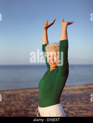 Porträt der gesunde ältere Frau praktizieren Yoga am Strand mit Exemplar. Passen alte kaukasische Frau trainieren im Freien bleiben. Stockfoto