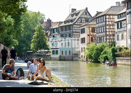 Leute sitzen am Ufer des Flusses, Viertel Petite France, Straßburg, Elsass, Frankreich Stockfoto