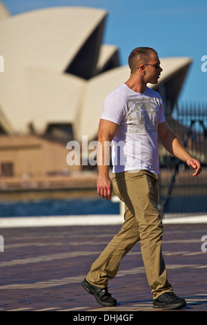 Junge Mann geht entlang der Uferpromenade am Circular Quay am Sydney Opera House im Hintergrund. Stockfoto