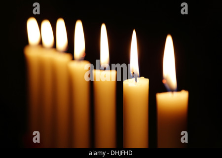 Reihe von brennenden Kerzen vor einem dunklen Hintergrund. Stockfoto