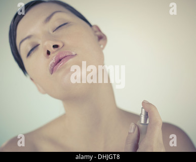 Eine junge Brünette Frau sprühen Parfüm am Hals Stockfoto