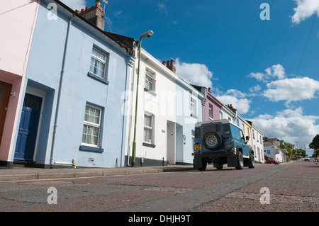 Land Rover Defender fahren auf der Straße entlang Pastell gemalt Reihenhäuser in Paignton, Devon, UK. Stockfoto