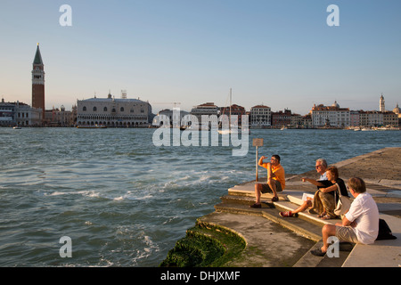 Menschen entspannen auf der Isola di San Giorgio Maggiore Insel mit Campanile-Turm in der Ferne, Venedig, Veneto, Italien, Euro Stockfoto