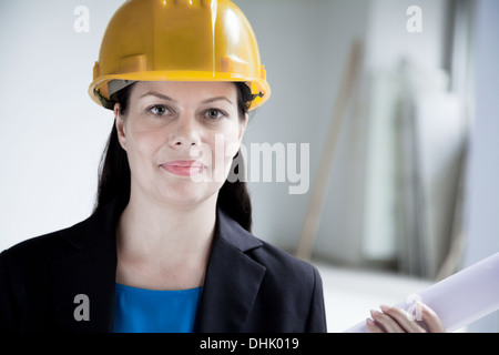 Porträt des lächelnden Architekten in einem Bauarbeiterhelm hält einen aufgerollten Plan drinnen, close-up Stockfoto