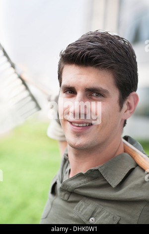 Porträt des jungen lächelnder Mann hält eine Harke auf einem Dachgarten in der Stadt Stockfoto