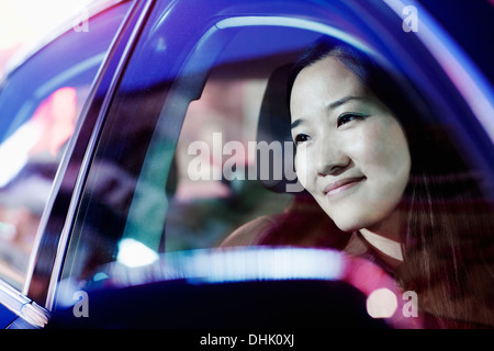 Lächelnde Frau, die auf der Suche durch Autofenster in das Nachtleben der Stadt reflektiert Licht Stockfoto