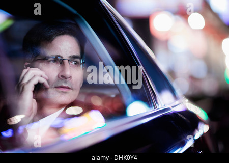 Geschäftsmann am Telefon und Blick aus dem Autofenster bei Nacht, reflektierte Licht Stockfoto
