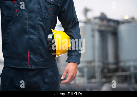 Mittelteil der junge Arbeiter, die mit einem gelben Bauarbeiterhelm im Freien mit Fabrik im Hintergrund Stockfoto