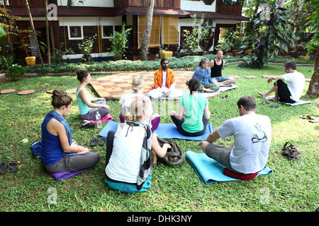 Yoga-Lehrerin sitzt in einem Resort-Garten mit seinen Schülern in Varkala, Indien zu meditieren. Stockfoto