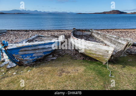 Alte und verlassene hölzerne Ruderboote auf einem Kiesstrand mit den Summer Isles und Skye in der Ferne. Stockfoto