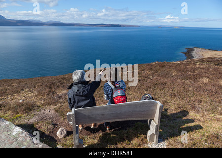 Eine Frau weist darauf hin den fernen Summer Isles, ihre Tochter sitzend auf einer Bank mit Blick auf Loch Broom. Stockfoto