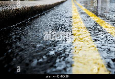 Regenwasser an der Dachrinne einer Straße mit dem Bordstein und doppelte gelbe Linien führen in die Ferne Stockfoto