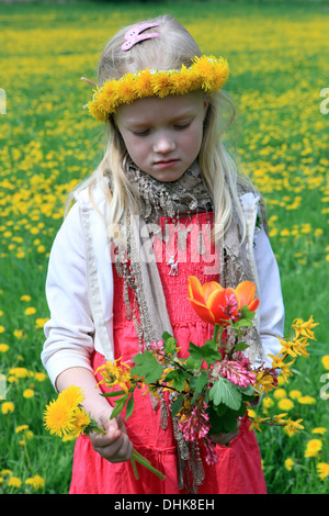 Trauriges junges Mädchen stehend in Spring Meadow mit Löwenzahn Kranz Kopf Löwenzahn Feld Frühlingsblumen Mai 8-9 Jahre altes Kind allein Vorderansicht trauriges Mädchen Stockfoto