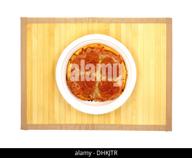 Draufsicht auf eine kleine Peperoni-Pizza auf einem Weißbuch Teller oben auf einer Holzlatte Tischset. Stockfoto