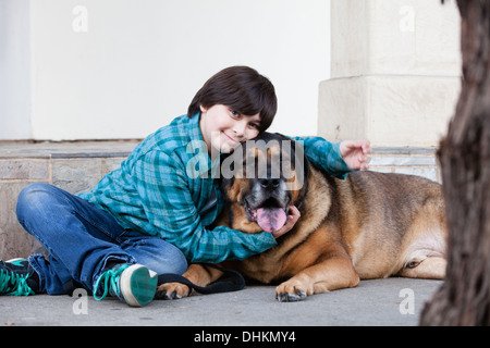 Ein 10 Jahre alter Junge und sein Hund auf dem Bürgersteig sitzen Stockfoto