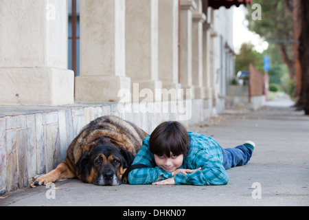 Ein netter 10 Jahre alter Junge und sein Hund liegend auf dem Bürgersteig Stockfoto