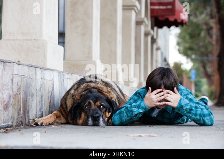 Ein 10 Jahre alter Junge und sein Hund liegend auf dem Bürgersteig spielen verstecken und suchen Stockfoto