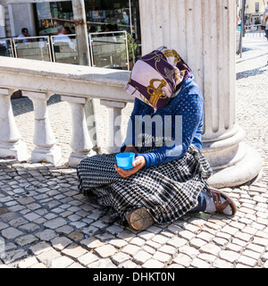 Alte Dame betteln um Geld, sitzen im Schatten mit einem blauen Plastikbecher. Allein, einsam. Blick von der Vorderseite. Nahaufnahme Stockfoto