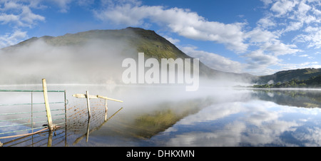 Panarama ein Zaun und Reflexion in Llyn Gwynant gehen. Der Nebel steigt über dem See teilweise verdeckt Gallt y Wenallt Stockfoto