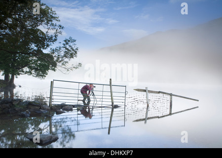 Fotograf in einem roten Mantel mit dem Fotografieren von einem Zaun und Reflexion in Llyn Gwynant, Snowdonia, Wales. Stockfoto