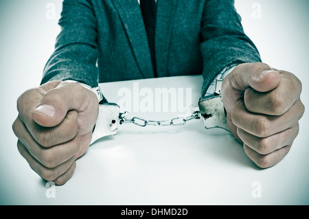 ein Mann in einem Anzug sitzt in einem Schreibtisch mit Handschellen in seine Handgelenke Stockfoto