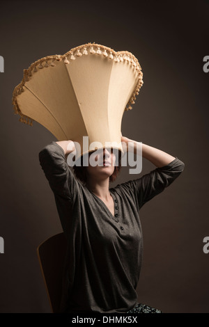 Eine Frau mit einem Lampenschirm auf ihrem Kopf trägt es wie ein Hut, UK (aus der unangemessenen Kopfbedeckungen "Serie) Stockfoto