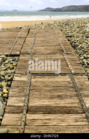 Holzsteg über eine umfangreiche Kiesel Meer Verteidigung am Newgale Strand mit Meer, Klippen und Kitesurfer in Ferne unscharf. Stockfoto