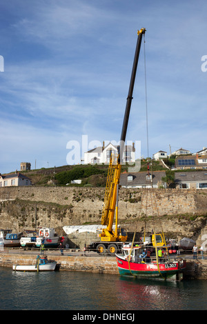 Ein großer gelber Kran heben eine rote Fischerboot aus Portreath Hafen während der Winter sich nähert, Cornwall England. Stockfoto