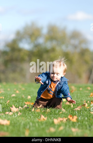 Ein ein-Jahr-alte Blondschopf in einer Jeansjacke Zahnspange selbst für einen Sturz während des Gehens in einem Feld auf ein warmer Herbsttag. Stockfoto