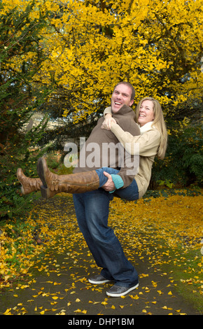 Vertikale Foto von Erwachsenen Brautpaar mit Mann mit seiner Frau eine Huckepack Reiten im Park während eines schönen Tages im Herbst Stockfoto