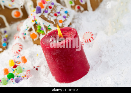 Closeup abgewinkelte horizontale Foto rote Kerze mit Lebkuchenhäuser, umgeben von Pulverschnee im Hintergrund Stockfoto