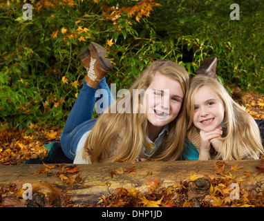 Horizontale Foto von zwei Schwestern, die Spaß beim liegen auf dem Boden im Park an einem schönen Herbsttag Stockfoto